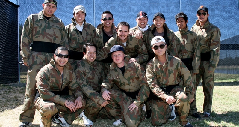Large group posing in front of a helicopter at Delta Force Paintball