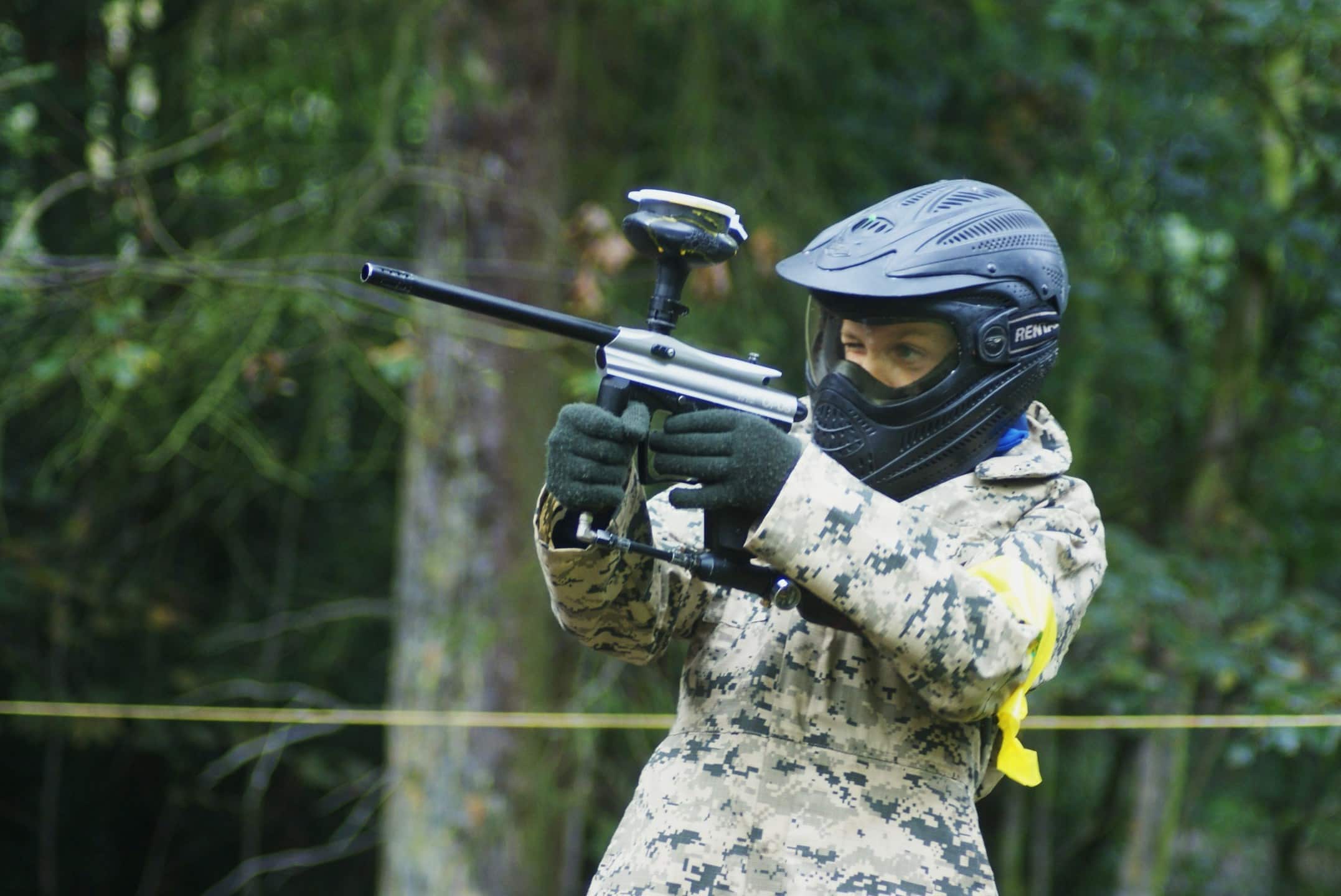 Young paintball player aiming in woodland