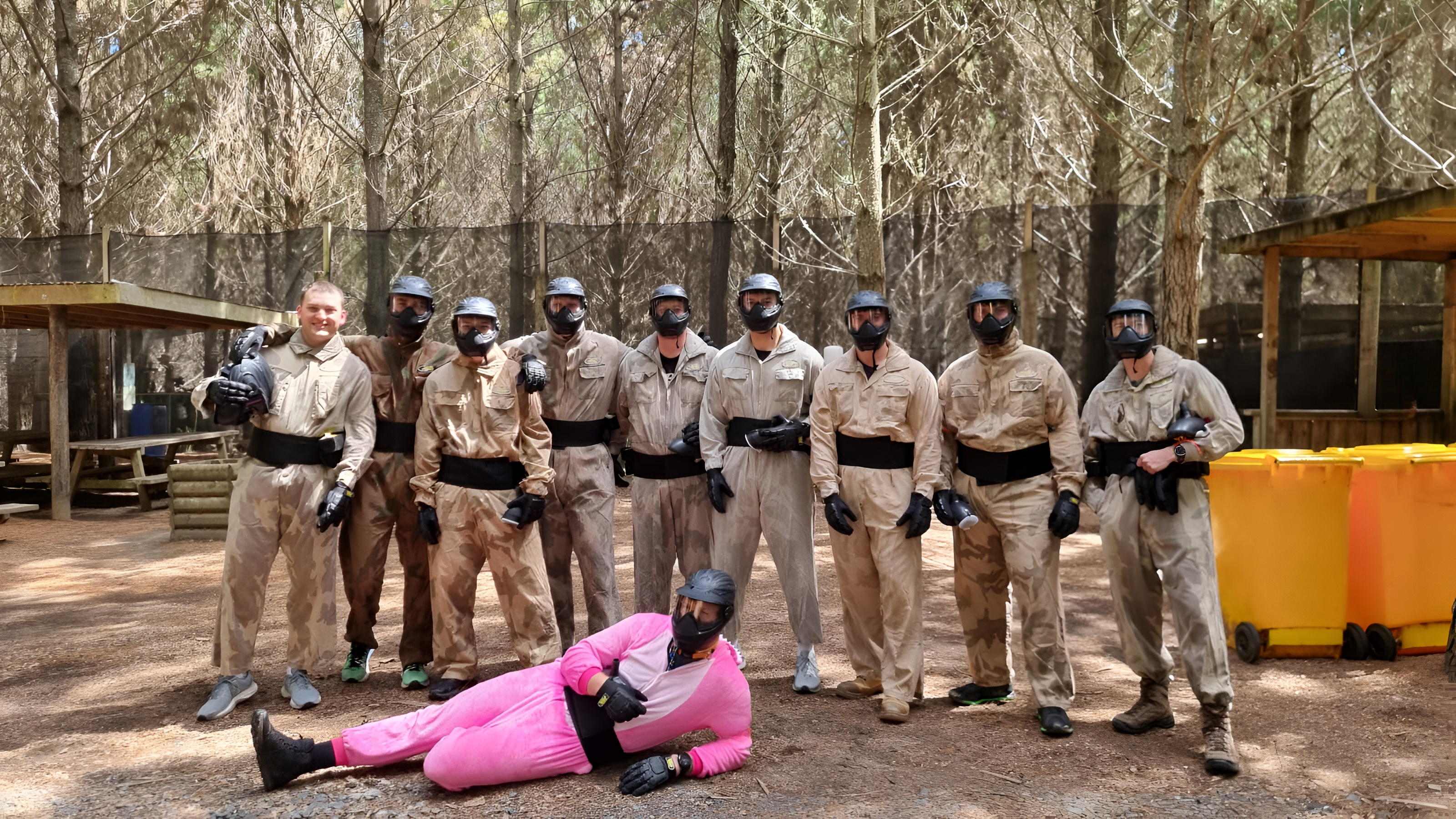 Stag do group in paintball kit posing in a woodland base camp