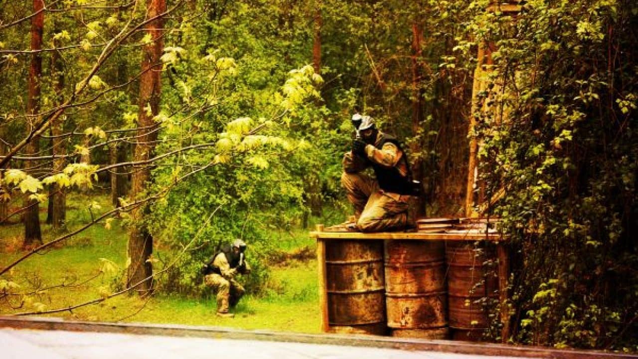 Delta Force player takes aim while crouching on barrels