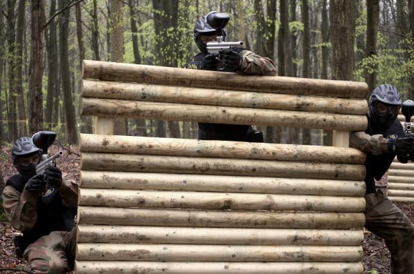 Three players aim around wooden barricade