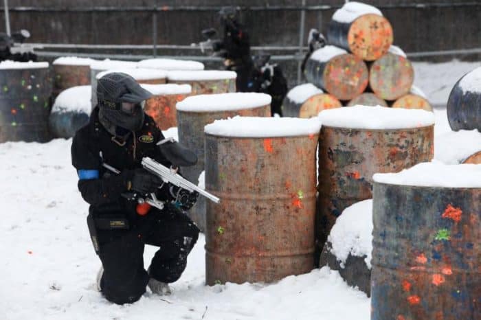 Paintball player takes cover behind snow-covered barrels