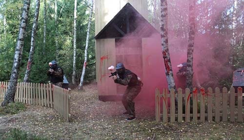 Three paintball players advance past blood-splattered fence