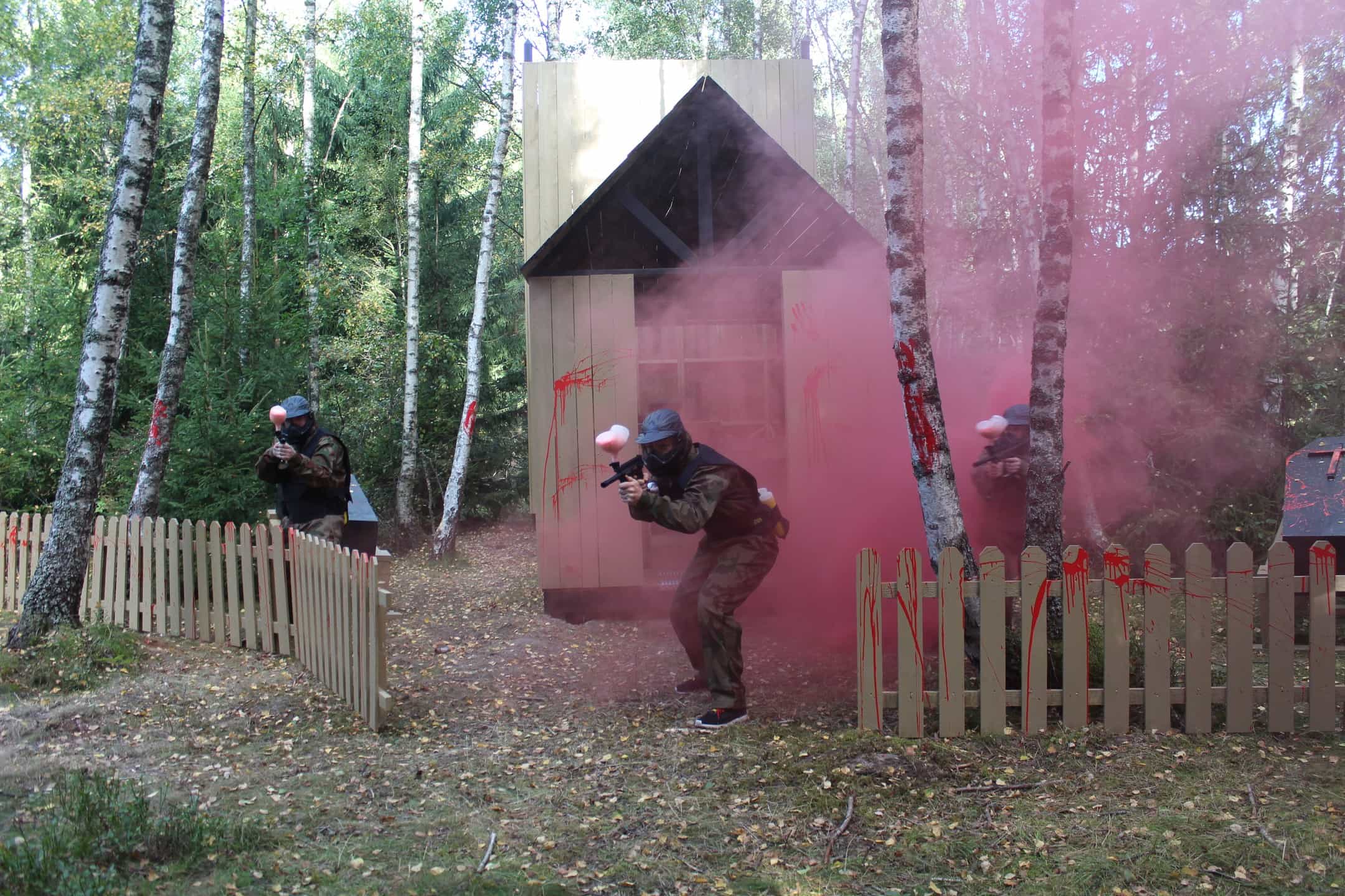 Three paintball players advance past blood-splattered fence